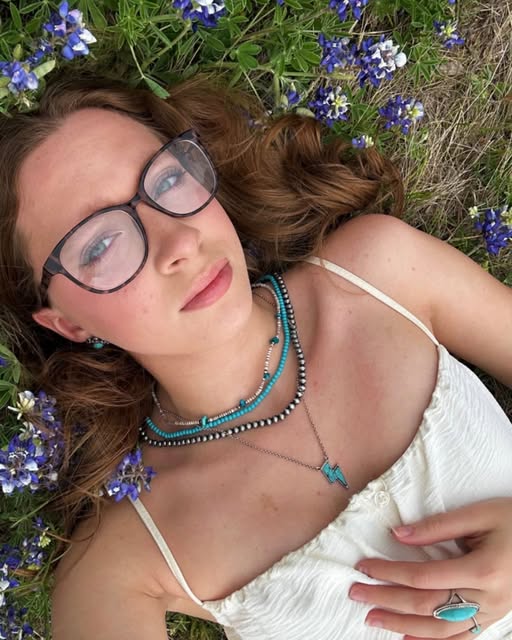 Portrait lying in bluebonnets, turquoise jewelry and a white top.